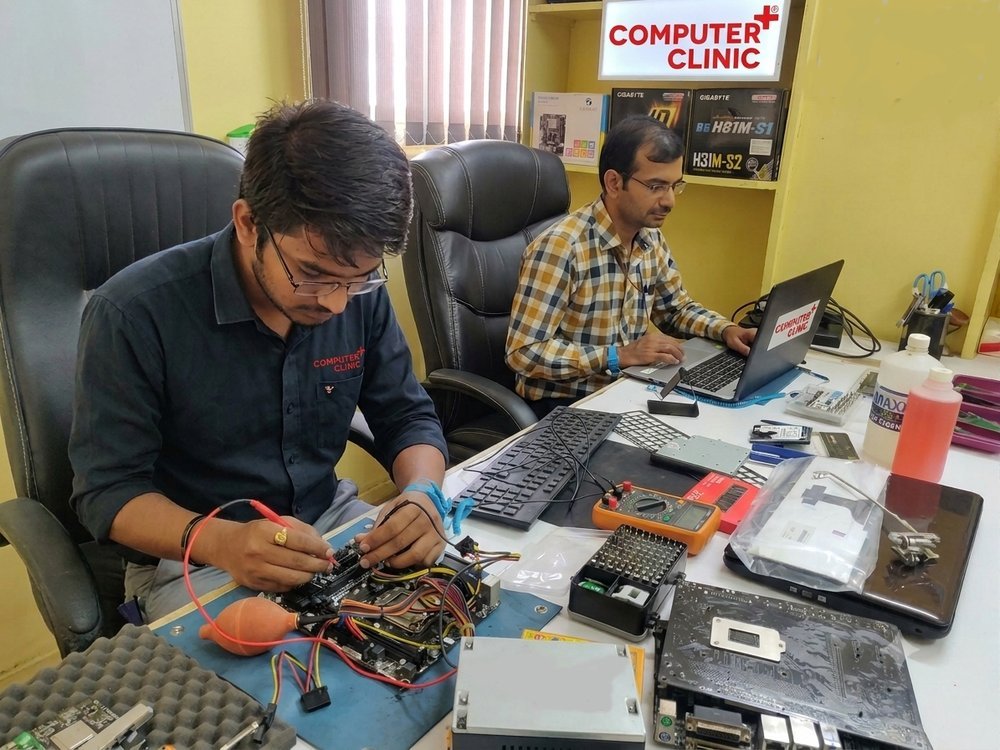 Computer Clinic technicians doing component-level motherboard repair at the Navrangpura workshop